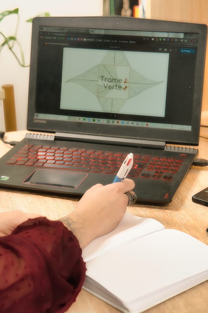 Ordinateur avec le logo de Trame Verte et un main qui prend des notes sur un carnet